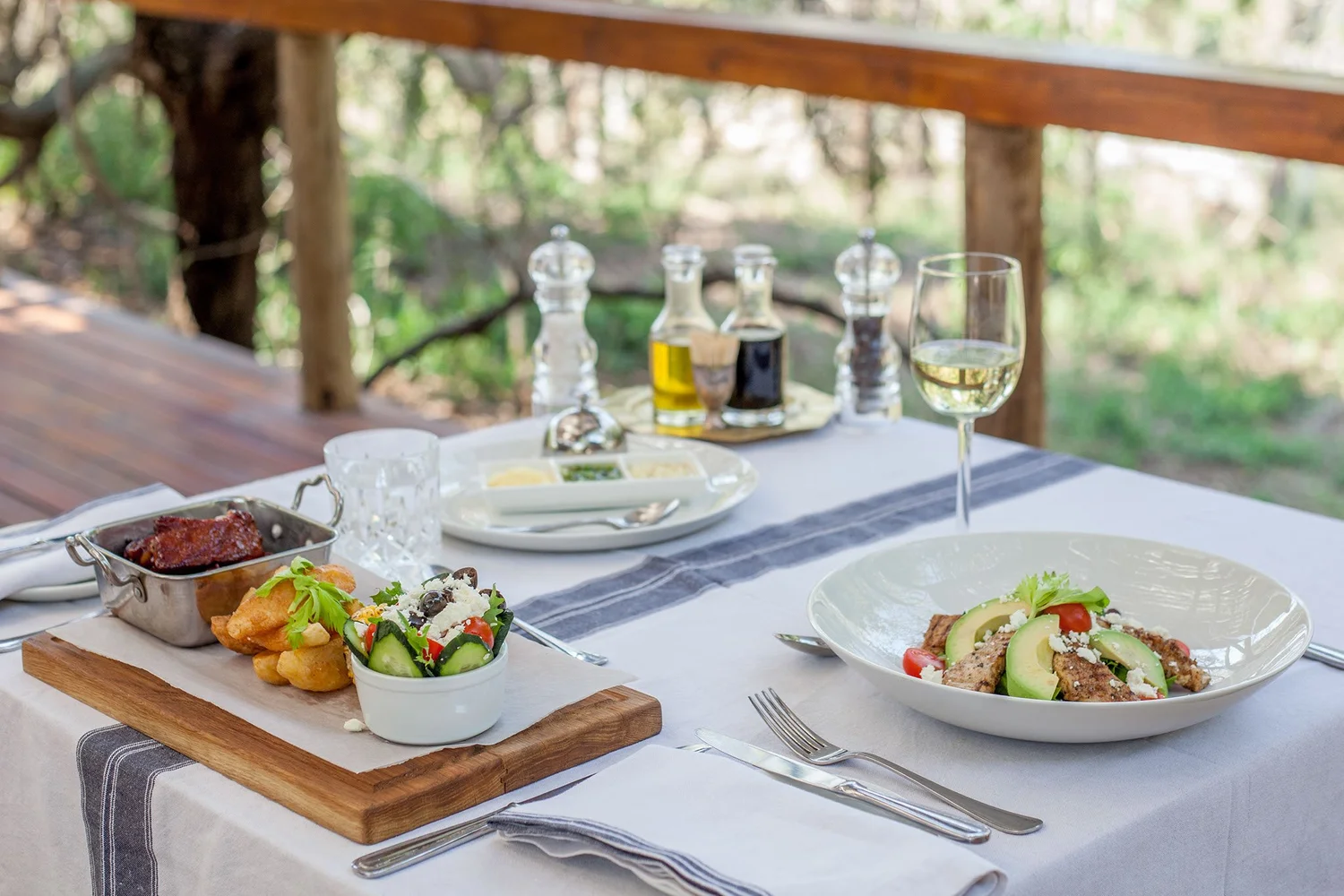 Table set for lunch on a shaded timber deck overlooking bush at a remote safari lodge